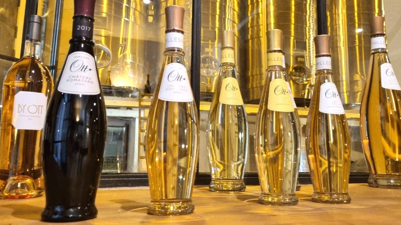 Bottles of Château d'Ott rosé stand before gleaming golden winery vats in the Var.